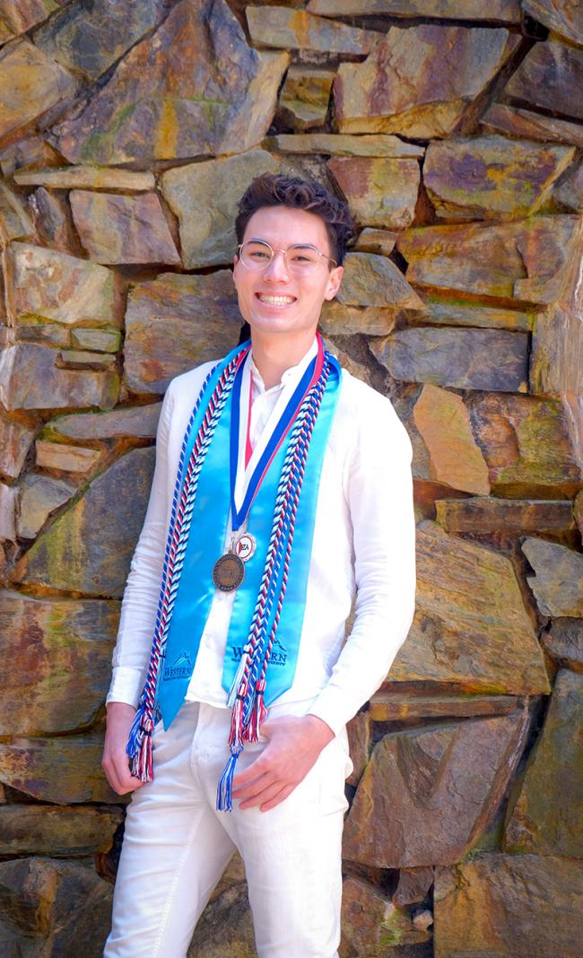 Nate Joe wearing a ribbon, braided tassels, and a medal in front of a stone wall