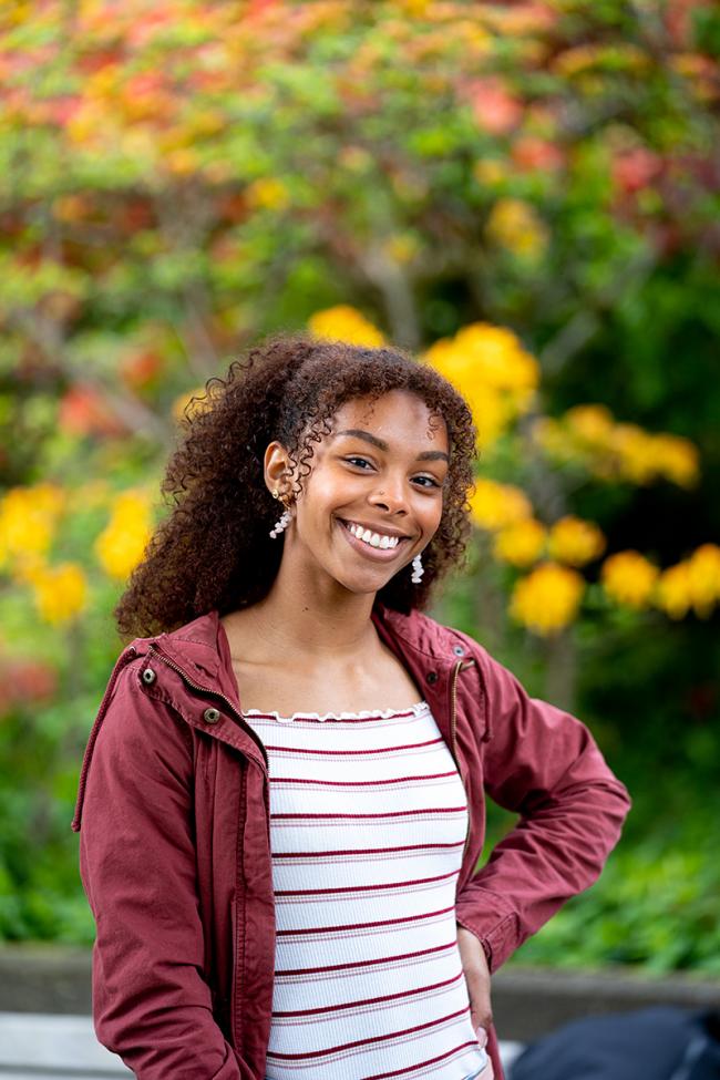 Aliyah Dawkins in a red jacket and striped shirt in front of flowers