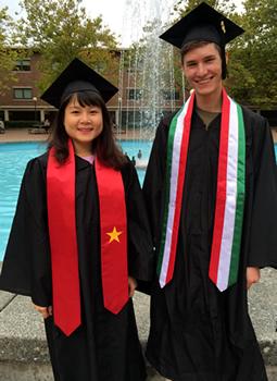 Two students in black cap and gown wearing stoles depicting the Mexican and Chinese flags.
